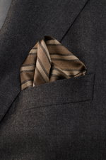 Brunello Cucinelli Silk Pocket Square grey brown/brown striped folded in a dark grey blazer pocket, close-up top view.  
<p>Subtle elegance for stylish appearances: With this noble pocket square in a subdued striped pattern, BRUNELLO CUCINELLI once again 