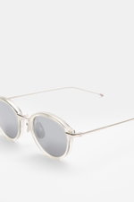 Thom Browne Sonnenbrille silbergrau, runde abgerundete Form, Metallrahmen mit Tricolore-Detail, getönte Gläser, seitliche Nahaufnahme schräg oben.