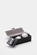 Thom Browne Sonnenbrille silbergrau mit abgerundeter Form, getönten Gläsern, Tricolore-Detail am Bügel, 100% UV-Schutz, im offenen Etui liegend, Seitenansicht.