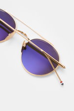 Thom Browne Sonnenbrille gold, rund mit filigranem Metallrahmen, blau verspiegelte Gläser, Tricolore-Detail am Bügel, von oben fotografiert.