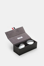 Thom Browne Sonnenbrille dunkelgrau in filigranem Metallrahmen mit runden, leicht verspiegelten Gläsern, Tricolore-Detail, 100% UV-Schutz, im offenen Hartschalenetui, von schräg oben fotografiert.