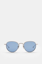 Frontale Nahaufnahme der Thom Browne Sonnenbrille hellgrau mit abgerundeter Form, transparentem Acetat-Rahmen, blauen Kunststoffgläsern und Tricolore-Detail am Bügel.