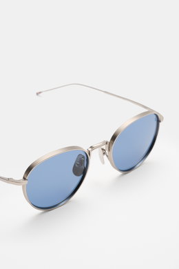 Thom Browne Sonnenbrille hellgrau mit abgerundeter Form, transparentem Acetat-Rahmen, blauen Gläsern, Tricolore-Detail, seitliche Nahaufnahme.