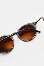 Nahaufnahme der Tom Ford Sonnenbrille 'Private Collection' schwarz/grau gemustert mit leicht gerundeter Silhouette und braunen Kunststoffgläsern, Acetat-Rahmen, 100% UV-Schutz, Filterkategorie 3, seitliche Perspektive.