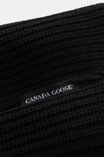 Close-up angled view of Canada Goose Wool beanie black showing chunky pure wool rib knit and woven label, robust fabric, turn-up style. 

<p>A must-have for the colder months: Don’t let bad hair days or cold winter days get to you with this beanie in pure