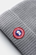 Close-up top-down view of a Canada Goose Wool beanie light grey showing chunky rib knit, pure wool fabric, and red circular logo patch on turn-up cuff.

<p>A must-have for the colder months: Don’t let bad hair days or cold winter days get to you with this