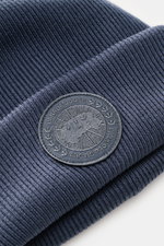 Canada Goose Wollmütze 'Arctic Toque' graublau aus reiner Wolle in feinem Rippstrick, doppellagig mit Umschlag und monochromem Weblabel, Nahaufnahme schräg von oben.