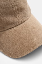 Nahaufnahme der 04651/ A trip in a bag Frottee Baseball-Cap 'Terry' taupe aus Baumwolle mit weichem Griff im Six-Panel-Stil, seitliche Perspektive.