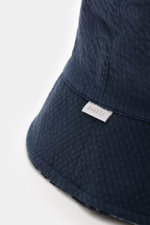 Nahaufnahme des navyfarbenen 04651/ A trip in a bag Wende-Frottee Bucket Hat, perspektivisch von der Seite, mit schmaler Krempe und Weblabel.