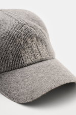 Close-up side view of the 04651/ A trip in a bag Cashmere Baseball-Cap grau meliert, showcasing fine knit cashmere, soft touch, mid-coarse texture, fine knit brim, and detailed front stitching of Milan Cathedral and Cortina mountain peaks. <p class="p1">L