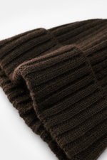 Nahaufnahme der Fedeli Cashmere Mütze dunkelbraun im Rippstrick mit weichem Griff und variablem Umschlag, fotografiert aus schräger Perspektive.