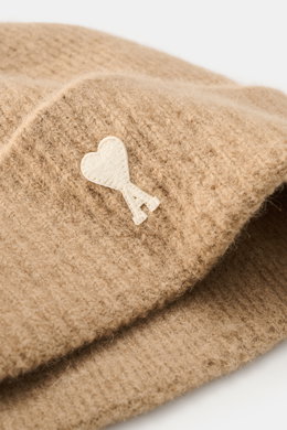 Ami Paris Beanie beige shown in close-up from a side angle, featuring a soft rib knit pattern, wide cuff, and a white heart logo patch; made of a mix of alpaca, wool, and microfiber with elastic quality and soft touch.