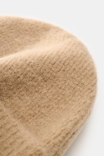 A close-up side view of the Ami Paris Beanie beige, showing its soft, classic rib knit pattern and wide cuff made from a mix of alpaca, wool, and microfiber, with elastic quality and a typical logo patch. In autumn and winter, this stylish beanie with the