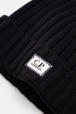 Close-up image taken from an angled top-down perspective showing the cuff with logo patch of the C.P. Company Merino beanie dark navy featuring pure merino wool, soft feel, classic ribbed knit pattern, and medium coarse knit texture.