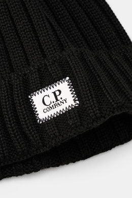 Close-up front view of C.P. Company Merino Mütze black showing pure Merino wool, soft touch, classic rib knit, medium knit texture, and folded cuff with logo patch.