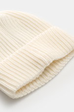 Nahaufnahme der C.P. Company Wollmütze offwhite, fotografiert von schräg oben, mit weichem Griff, reiner Schurwolle, klassischem Patentstrickmuster, mittelgroßem Strickbild und Umschlag mit Linsen-Detail.