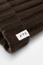 Close-up, angled view of the FTC Cashmere beanie dark brown showing its rib knit brioche pattern, medium-fine knit, and variable brim with FTC woven label, made from pure, very soft Fair Trade cashmere, a luxurious winter accessory no wardrobe should be w
