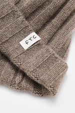 Close-up front view of the FTC Cashmere Beanie Taupe showing its ribbed knit pattern and narrow cuff with FTC woven label, made from pure cashmere with a very soft feel and medium-fine knit texture.