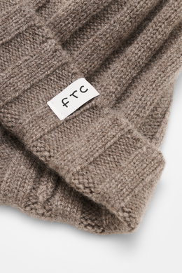 Close-up front view of the FTC Cashmere Beanie Taupe showing its ribbed knit pattern and narrow cuff with FTC woven label, made from pure cashmere with a very soft feel and medium-fine knit texture.