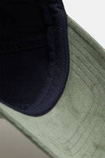 Close-up view of the inside and brim of the 04651/ A trip in a bag Corduroy baseball cap sage, showing corduroy made of elastic cotton, characteristic texture, classic six-panel design, and adjustable closure in navy and sage colors.