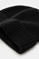 Nahaufnahme der 04651/ A trip in a bag Cashmere Mütze schwarz mit breitem Umschlag und markantem Patentstrickmuster, mittelfeines Strickbild, sehr weicher Griff aus reinem Cashmere, fotografiert aus schräger Perspektive.