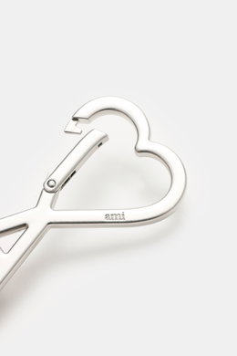 Ami Paris Schlüsselanhänger silber shown from a close-up top angle, featuring a heart-shaped AMI-logo carabiner with "ami" engraving, approx. 8 x 5 cm. <p>Unisex Accessoire von AMI PARIS: Dieser praktische Begleiter mit dem markentypischen 'A' mit Herz hä