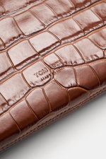 Nahaufnahme der braunen Tom Ford Tasche braun aus edlem Kalbleder im Reptilien-Look mit dezenter Logo-Prägung, fotografiert von oben schräg.