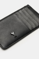 Ami Paris Kartenetui schwarz shown from a slightly angled top-down view, featuring finely grained black calf leather, five card slots, a central zip compartment, a large back pocket, and a front logo heart-shaped "A". <p>Stilvolles Accessoire für den Allt
