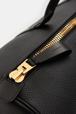 Tom Ford Weekender schwarz, Nahaufnahme von genarbtem Kalbleder und goldfarbenem XXL-Reißverschluss, Perspektive von oben schräg.
