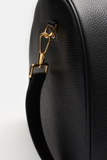 Nahaufnahme des Tom Ford Weekender schwarz aus genarbtem Kalbleder, Fokus auf goldfarbene Oversized-Hardware und Tragegriff, seitliche Perspektive.