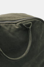 Nahaufnahme des olivgrünen 04651/ A trip in a bag Weekender '356 Bag' aus Veloursleder mit Reißverschluss und Logo-Prägung, von schräg oben fotografiert.