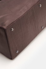 Nahaufnahme der Unterseite des 04651/ A trip in a bag Weekender 'Nubuck' bordeaux aus edlem Nubukleder mit robusten Metallfüßen, brünierten Details und geschmeidiger Oberfläche, fotografiert aus schräger Perspektive.