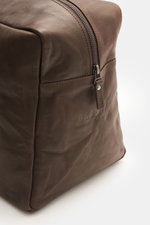 Nahaufnahme des braunen 04651/ A trip in a bag Weekender 'Nubuck' aus feinem Nubukleder mit gebranntem Reißverschluss-Pull-Tag und seitlicher Logo-Prägung, Perspektive von vorne rechts oben.