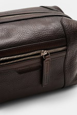 Officine Creative Toiletries bag dark brown shown from a close-up front angle, highlighting fine grained calfskin, silver hardware, zippered outside compartment, and embossed logo. A luxurious travel essential by OFFICINE CREATIVE: elegant toiletries bag 