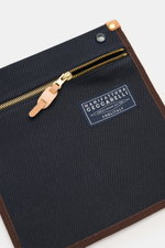 Nahaufnahme des Manifattura Ceccarelli Rucksack 'Laptop' navy aus reiner Baumwolle mit goldfarbenem Reißverschluss, Logo-Patch und braunen Kanten, frontal fotografiert.