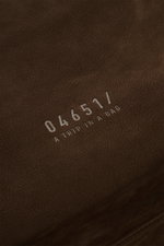 Nahaufnahme des dunkelbraunen Veloursleders mit silberner 04651/-Prägung des 04651/ A trip in a bag Weekender '356 Bag'.