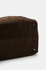Detailaufnahme von der Unterseite des dunkelbraunen 04651/ A trip in a bag Weekender '356 Bag' aus Veloursleder mit Metallfüßchen.