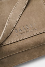 Nahaufnahme des weichen Nubukleders mit silberfarbener Logo-Prägung des 04651/ A trip in a bag Rucksack 'Hybrid Tote' taupe, Detailansicht mit Tragegriff.