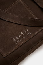 Nahaufnahme aus schräger Perspektive des dunkelbraunen 04651/ A trip in a bag Rucksack 'Hybrid Tote' aus weichem Nubukleder mit Logo-Prägung.