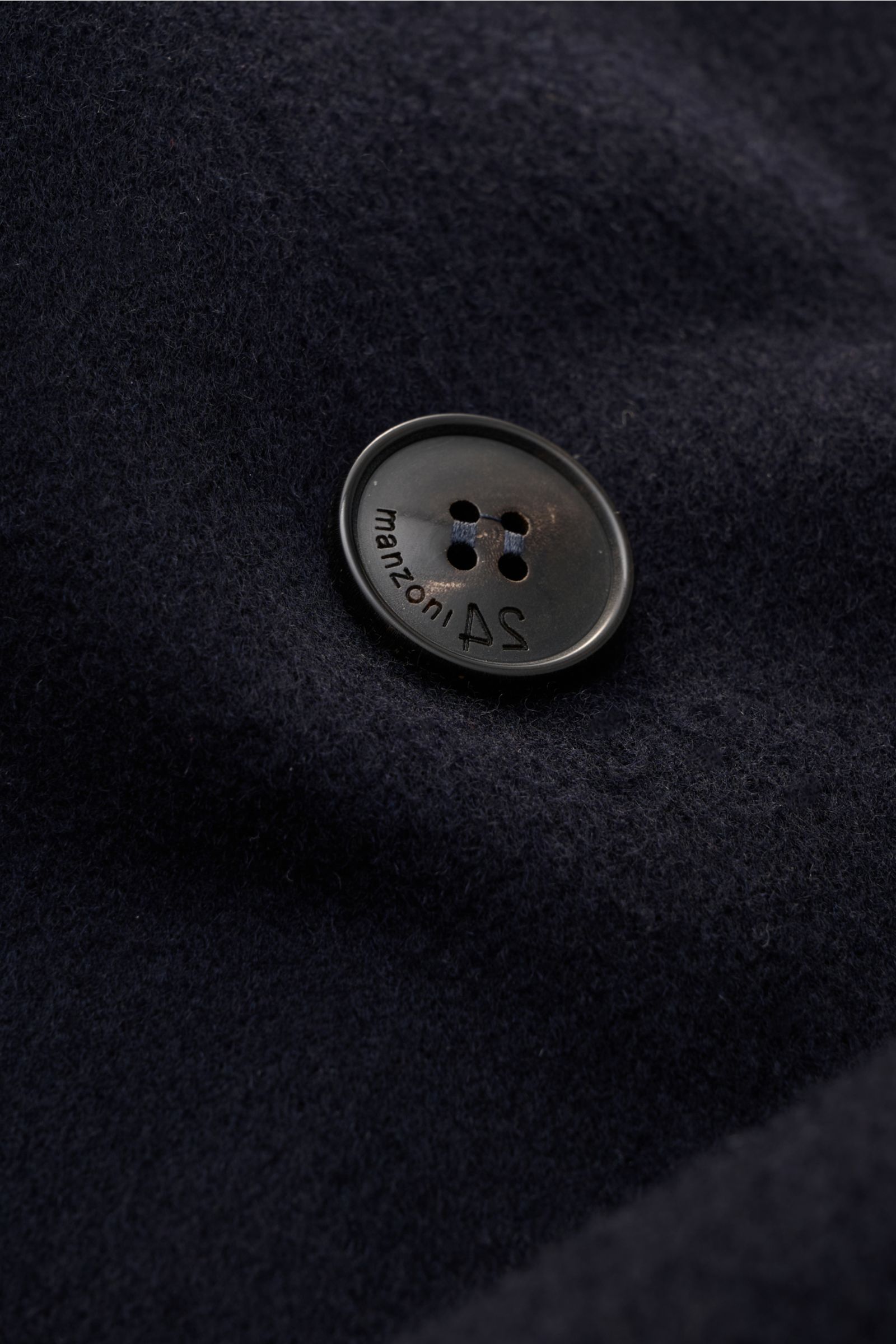 Nahaufnahme eines schwarzen Knopfs mit Prägung auf dunkelblauem Wollstoff, Detailansicht des Manzoni 24 Mäntel - U640.