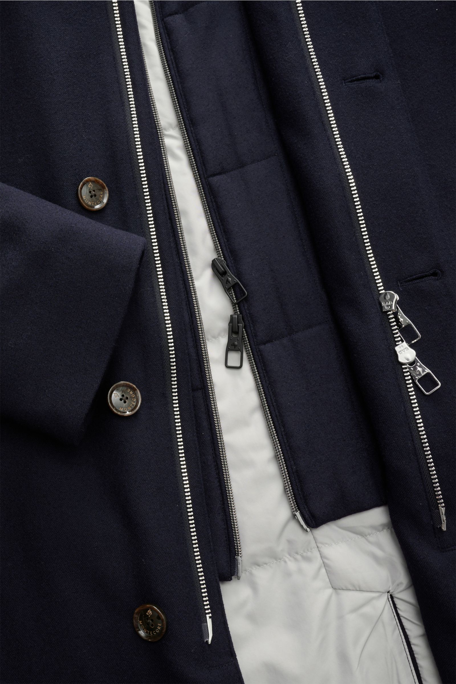 Close-up top-down view of the Montecore Short down coat, navy, showing the elastic virgin wool fabric, detachable double front with zippers, buttons, and lightweight down lining.

An elegant essential for winter: This down jacket by MONTECORE is warm a