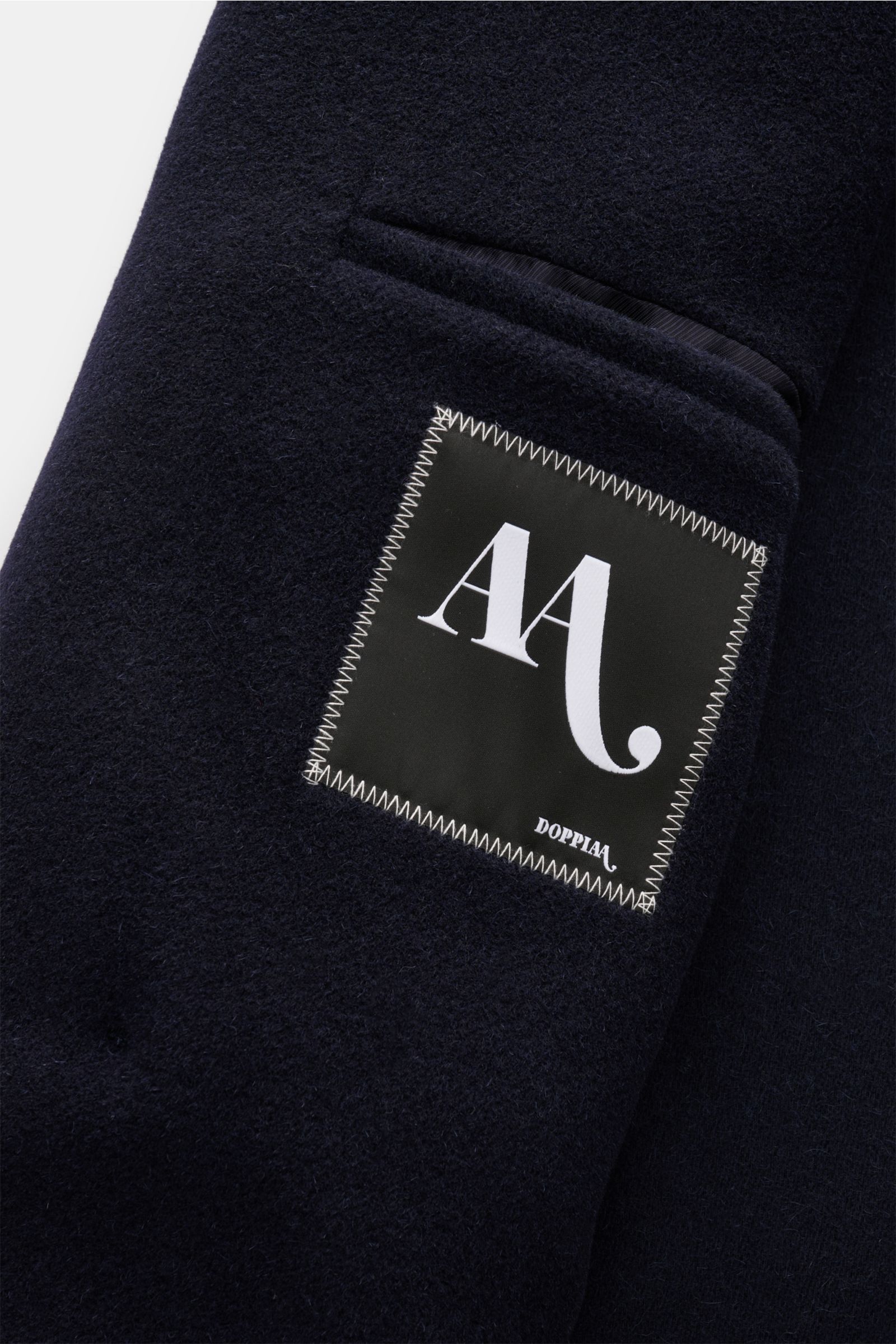 Nahaufnahme des Doppiaa Mantels 'Aajax' navy, zeigt das weiche Material aus Alpaka- und Schurwolle mit Label und Brusttasche.