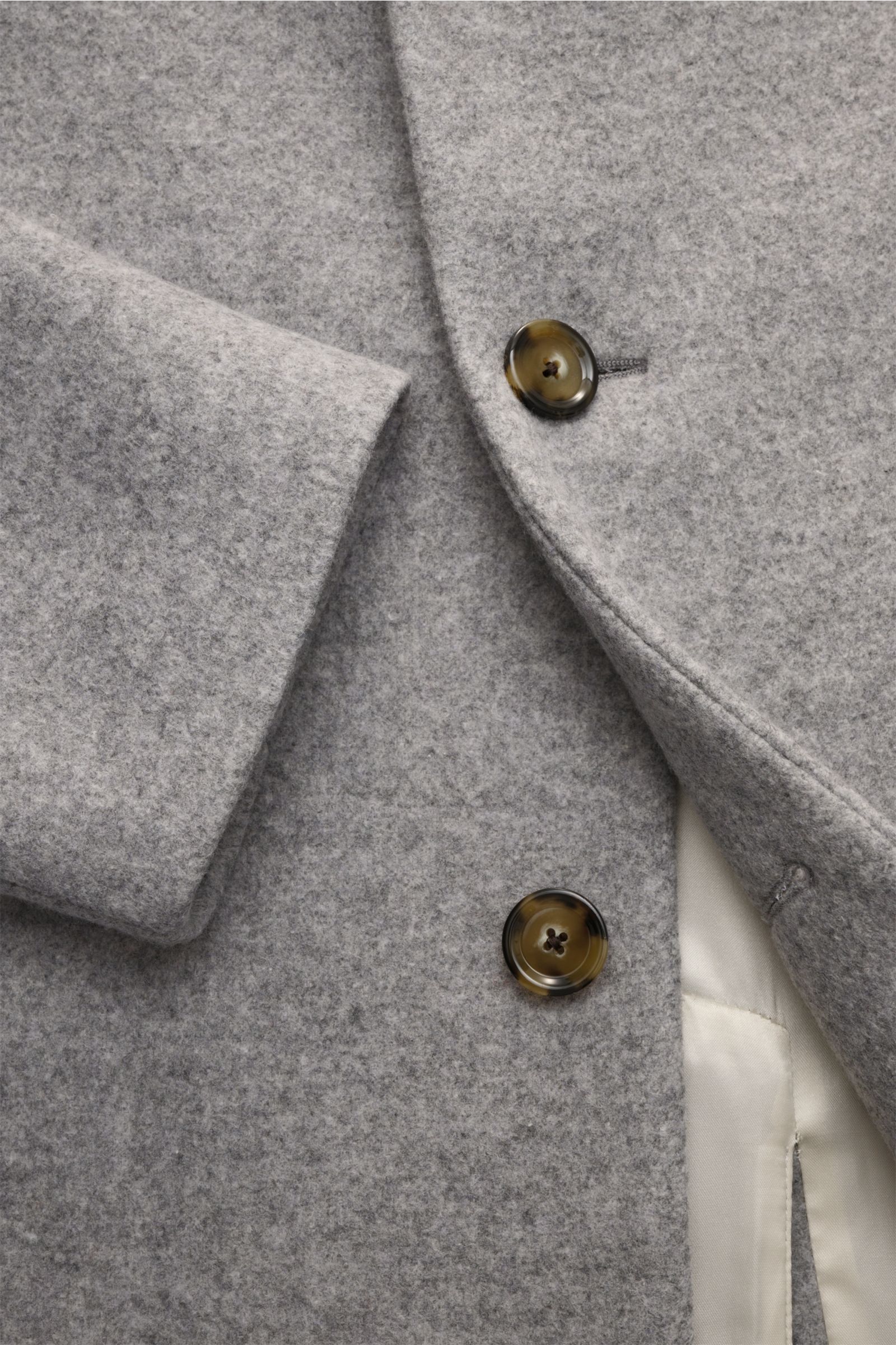 Lardini Mantel grau close-up showing soft wool fabric, three-button front, lapel with flower pin, slanted welt pockets, and tonal lining from a front angle.  
Ein perfekter Mantel vereint zeitloses Design, eine klassische Silhouette und erlesene Materi