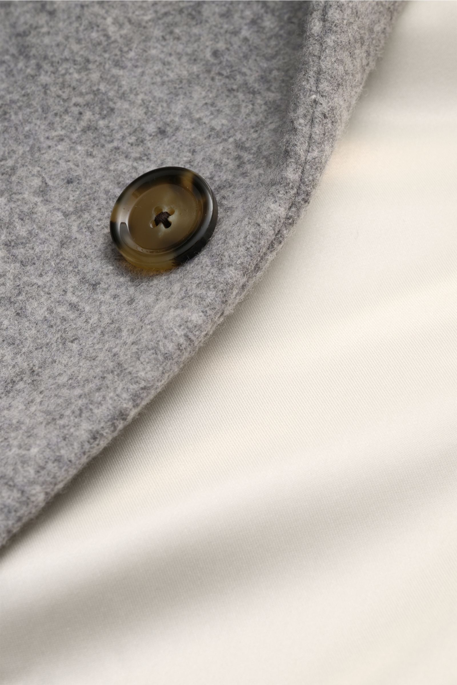 Close-up of Lardini Mantel grau showing the textured grey wool fabric with a brown button and smooth cream lining, photographed from above.