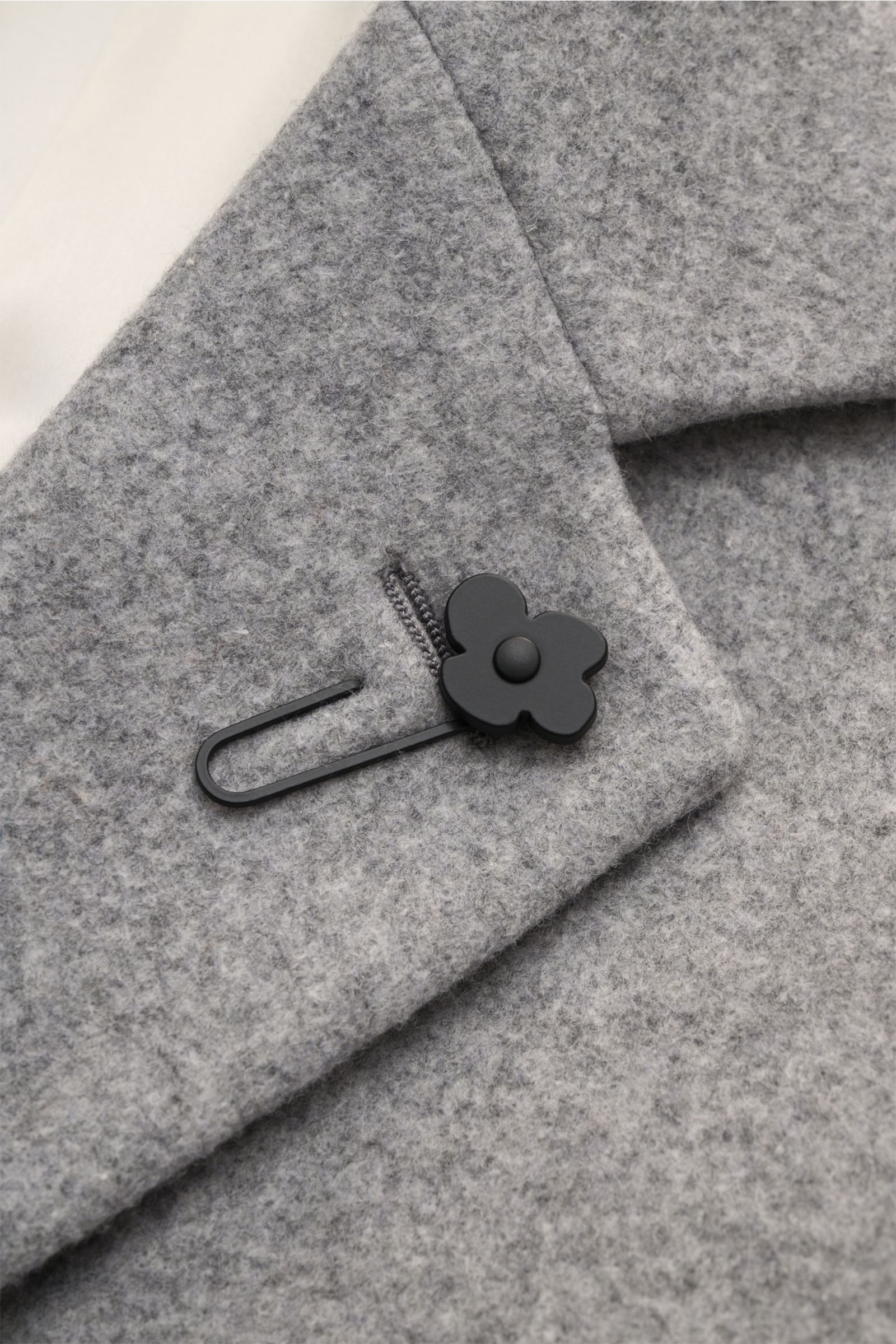 Close-up front detail of Lardini Mantel grau showing grey wool fabric, lapel with signature black flower pin from a top angle.

Description: Ein perfekter Mantel vereint zeitloses Design, eine klassische Silhouette und erlesene Materialien wie Cashmere