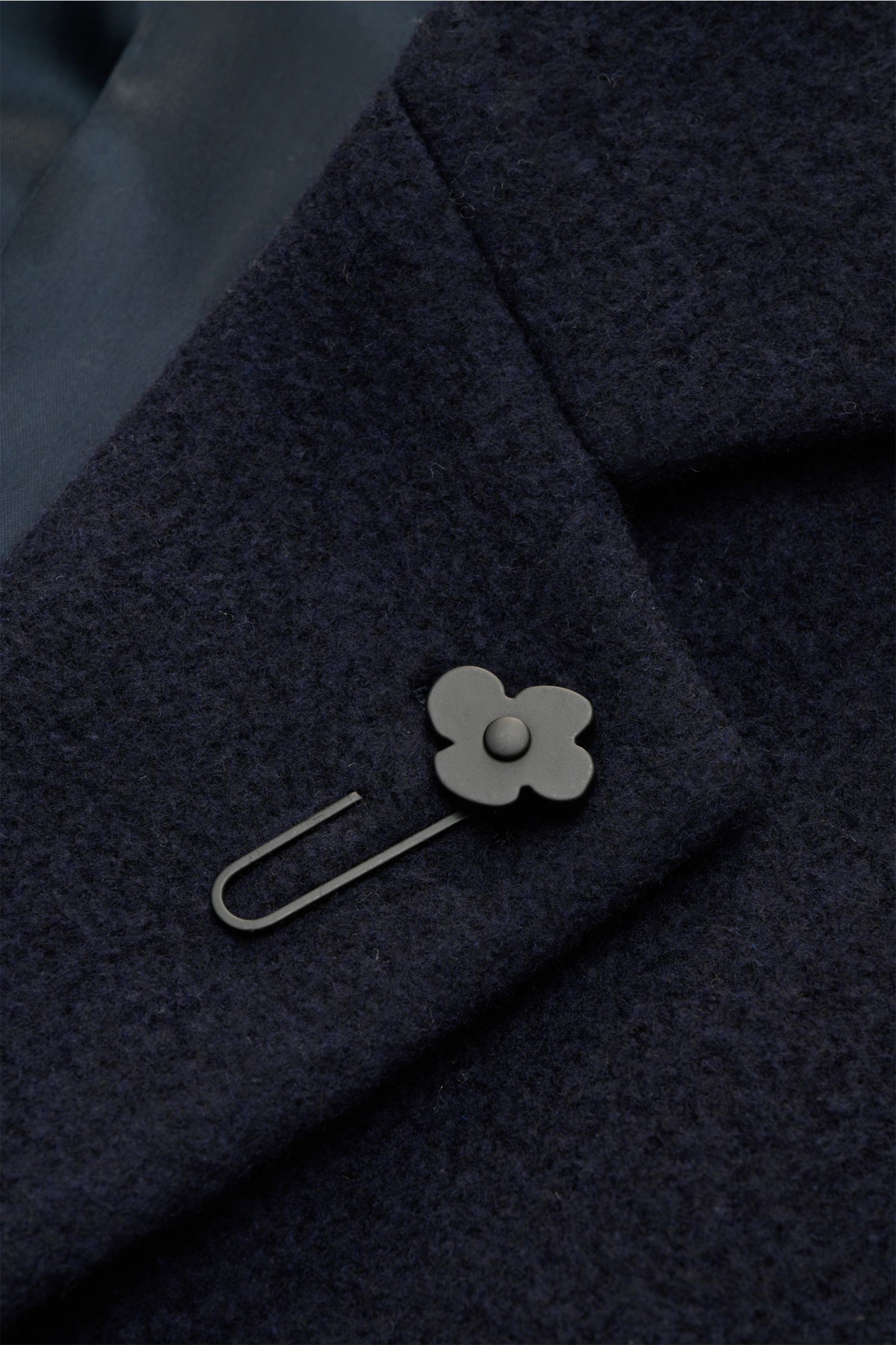 Close-up front view of Lardini Mantel navy showcasing the textured wool fabric, lapel with signature flower pin, and soft lining.

Ein perfekter Mantel vereint zeitloses Design, eine klassische Silhouette und erlesene Materialien wie Cashmere, Seide un