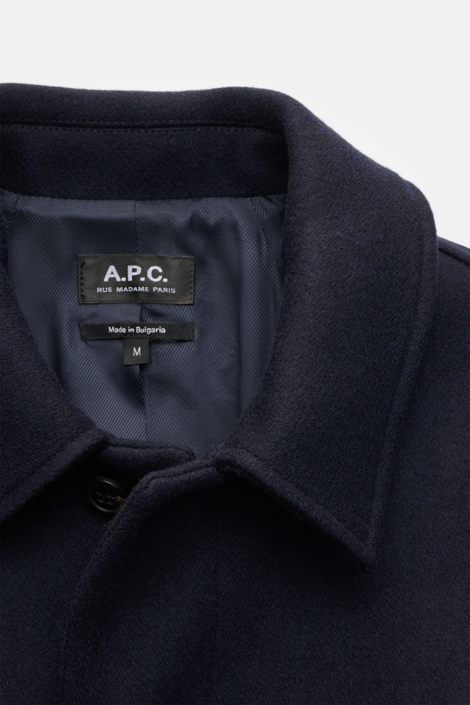 Close-up front view of the collar and label of the A.P.C. Mantel 'Mac Auster' navy, a stately coat made from a wool and microfiber blend with a felted, firm texture, featuring a regular fit, concealed five-button placket, turn-down collar, raglan sleeves,