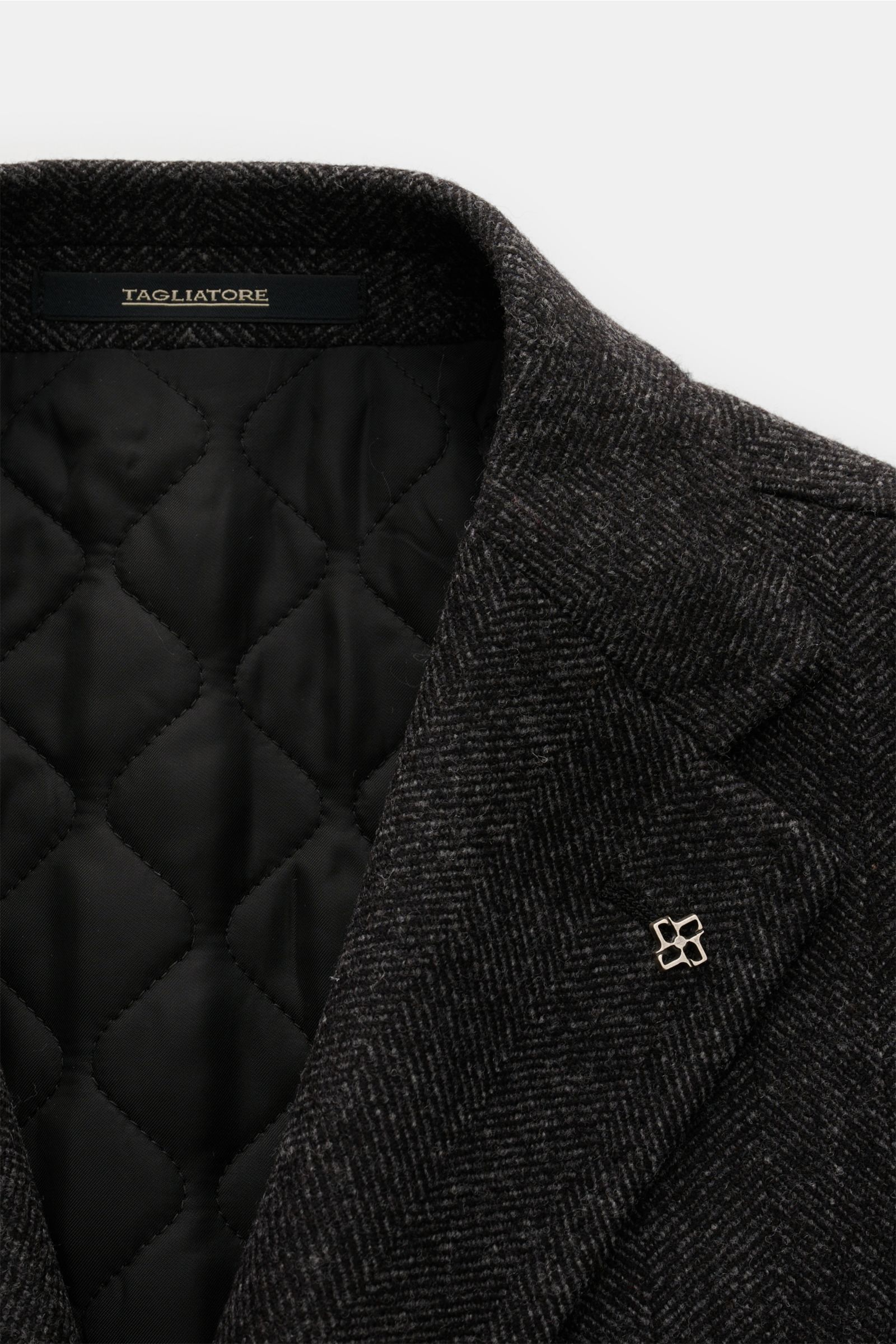 Nahaufnahme des halb gefütterten Tagliatore Mantels schwarz/grau gemustert mit Fischgrat-Webmuster, Reverskragen und gesteppter Innenseite.