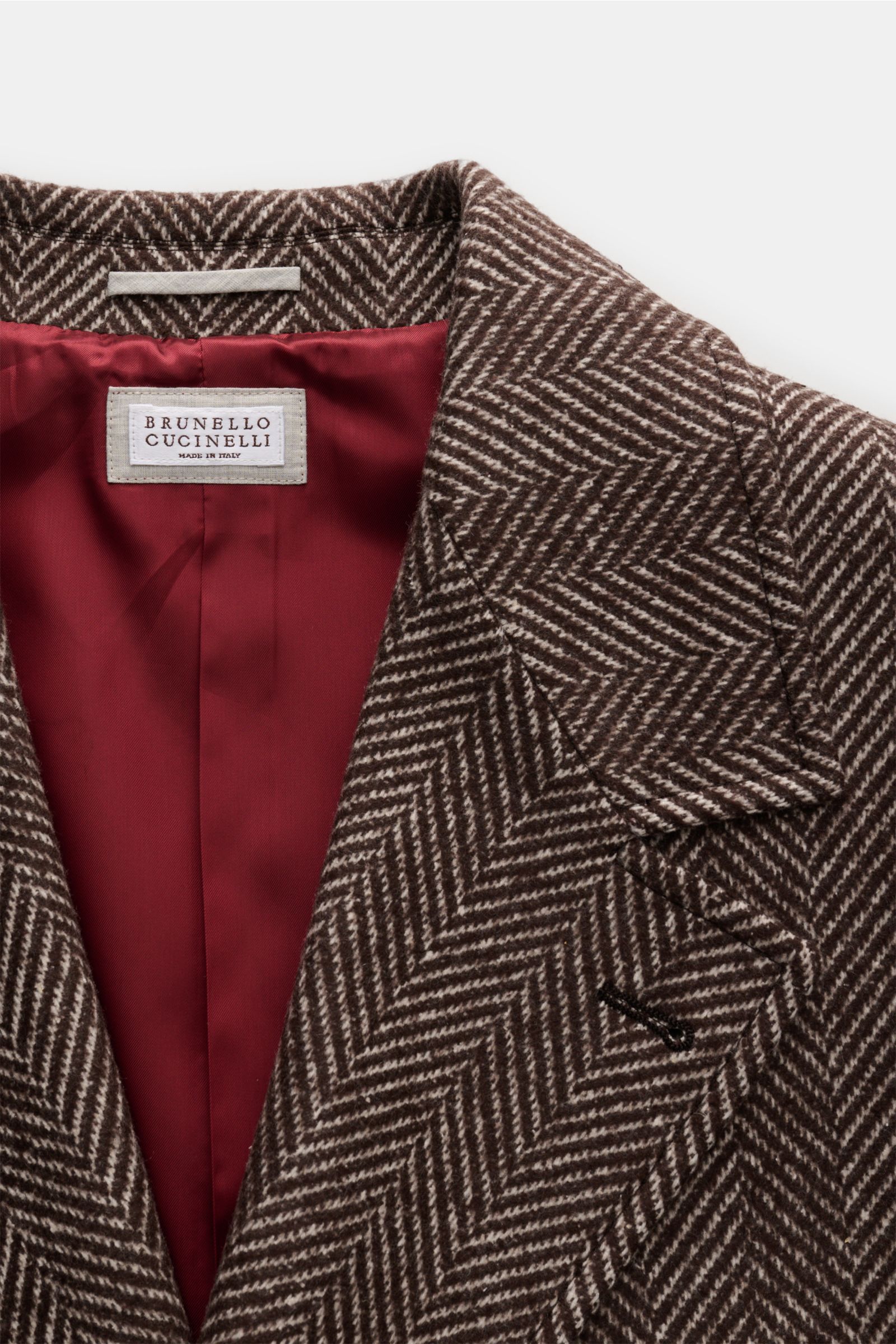 Brunello Cucinelli Mantel dunkelbraun/offwhite gestreift, Fischgrat-Webmuster, breiter Reverskragen, dre Knopf-Stil, innen rot, Detail von oben fotografiert.