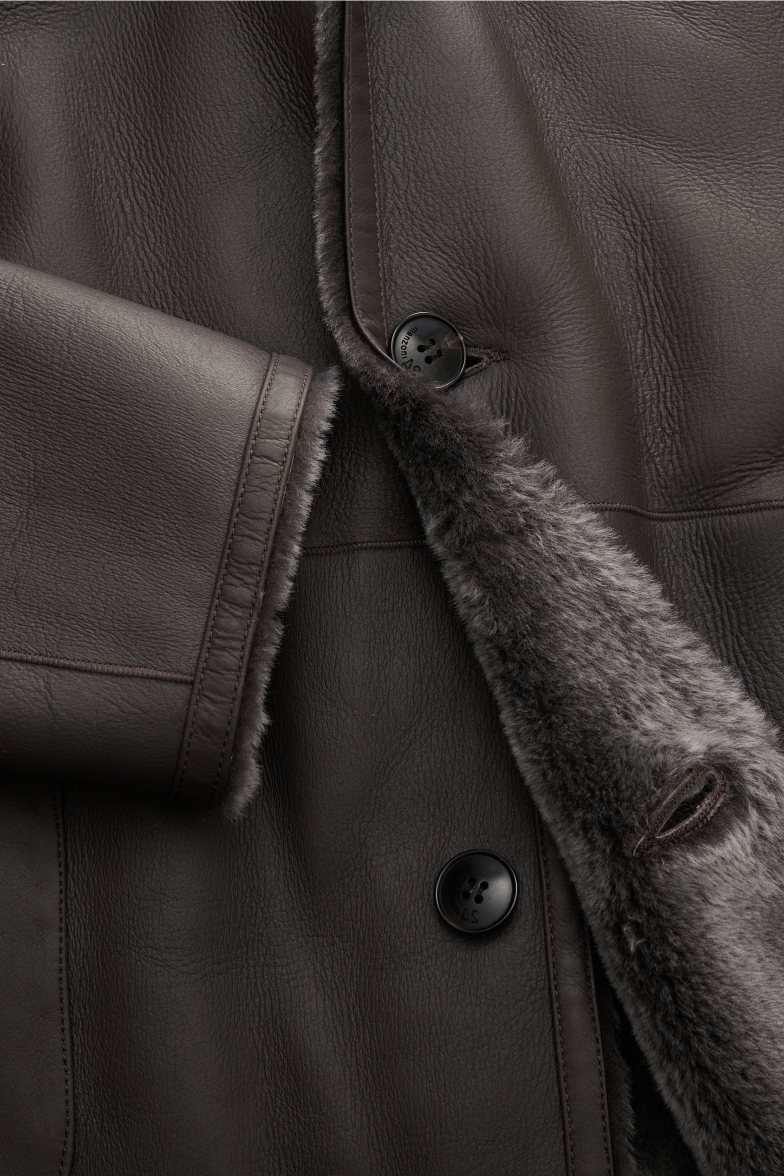 Manzoni 24 Lammfellmantel graubraun, Nahaufnahme von Innen- und Außenseite mit weichem Lammfell, Reverskragen und Drei-Knopf-Leiste.